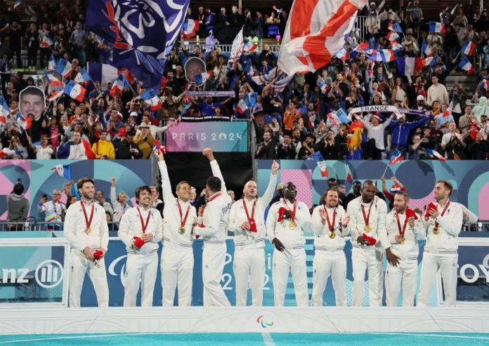 Ten blind football players wearing France's white uniform celebrates on the podium in front of many fans